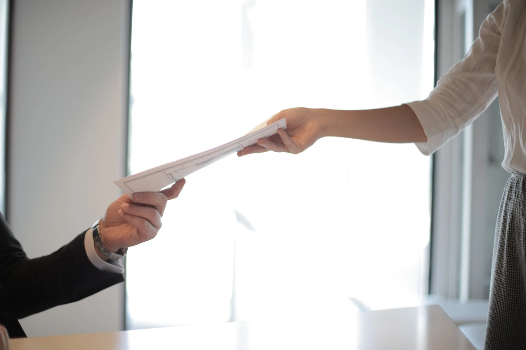 Two people handing paper documents to one another in an office